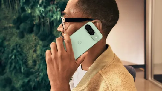 A person wearing glasses and a vest holds a mint-colored Pixel phone to their ear.